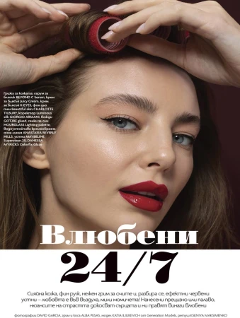 Close-up beauty shot of a woman with fair skin, wearing red lipstick, and styling her hair with rollers against a dark background.