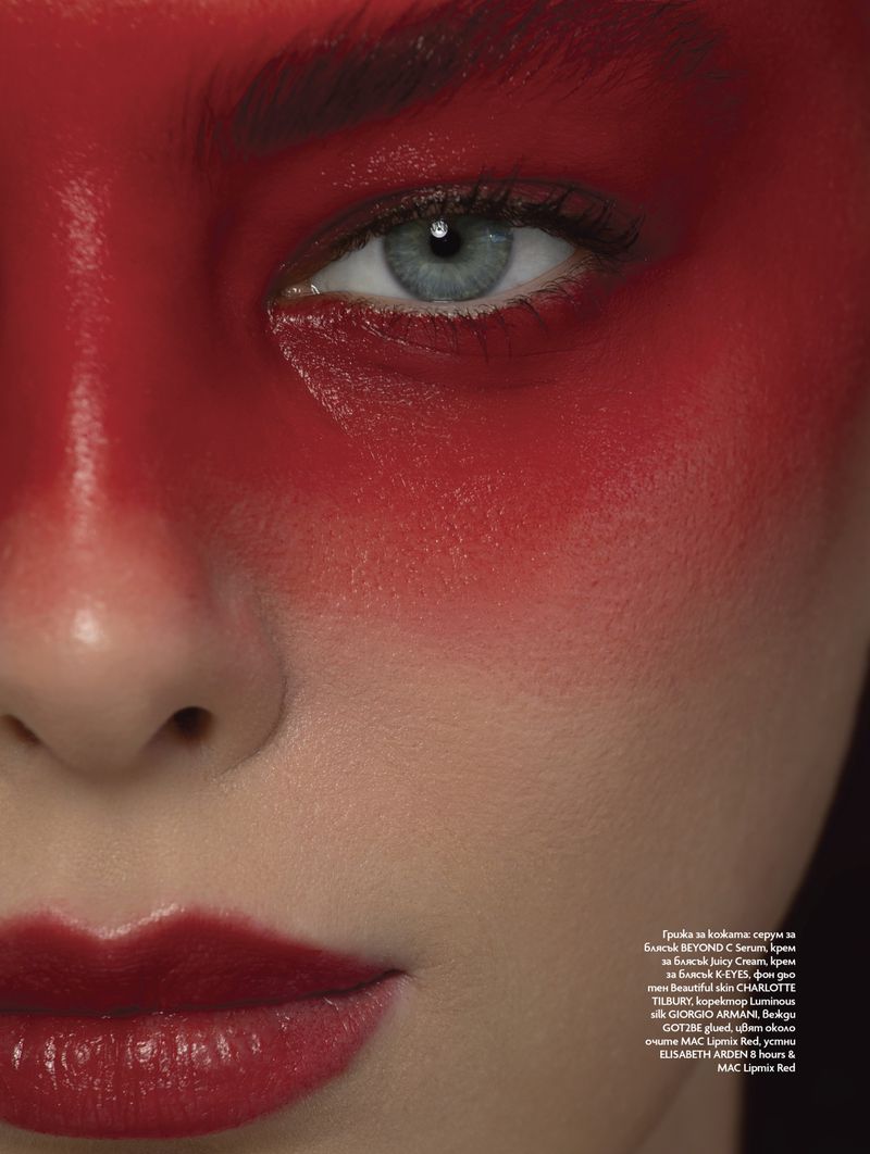 Close-up portrait of a fair-skinned adult female with red face paint and red lipstick in a photo studio setting.