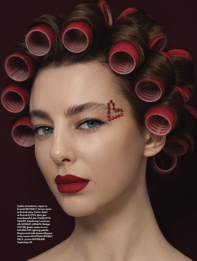 Portrait of a woman with red lipstick and hair rollers in a photo studio setting for beauty advertisement or fashion editorial.