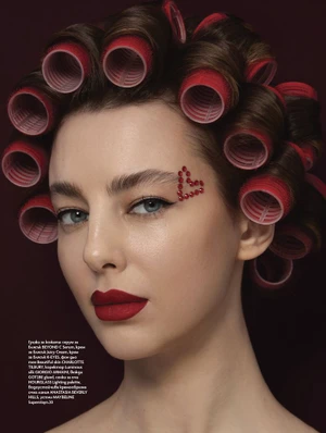 Close-up portrait of a woman with red hair rollers, red lipstick, and rhinestone heart makeup for Elle Bulgaria.