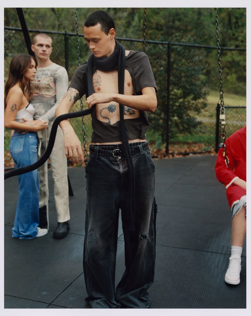An editorial fashion shot of a group of young adults in an urban park setting with playground equipment.