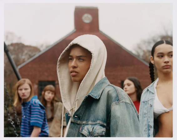 A young person in a cream hoodie and denim jacket stands in the foreground, with four other people slightly out of focus behind them.