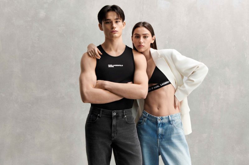 A young couple poses for a fashion-editorial studio shot wearing Karl Lagerfeld branded clothing in front of a neutral grey backdrop.