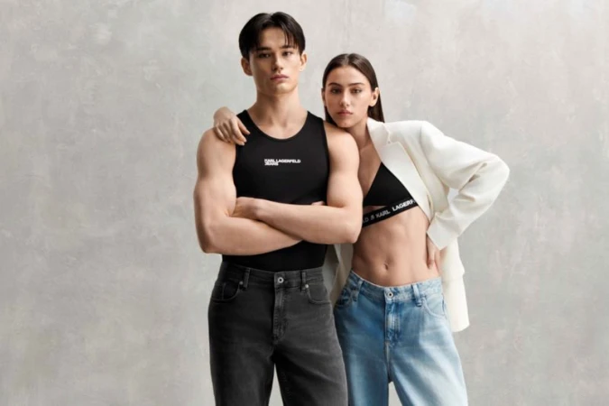 A young couple poses for a fashion-editorial studio shot wearing Karl Lagerfeld branded clothing in front of a neutral grey backdrop.