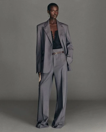 Model standing against a plain grey studio backdrop wearing an oversized grey suit jacket and matching trousers.