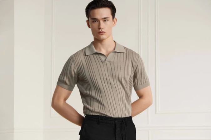 Model Alex Schlab wearing a ribbed beige polo shirt and black trousers against a neutral wall for Karl Lagerfeld.