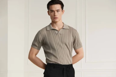 Model Alex Schlab wearing a ribbed beige polo shirt and black trousers against a neutral wall for Karl Lagerfeld.