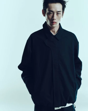 Portrait of a slender Asian male model in a dark blue jacket against a graduated blue background in a clean studio fashion shot.