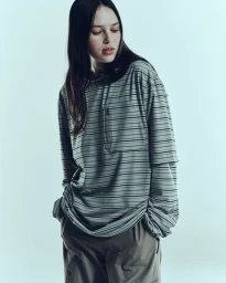 Woman with long dark hair wearing a striped long-sleeve t-shirt against a plain light background