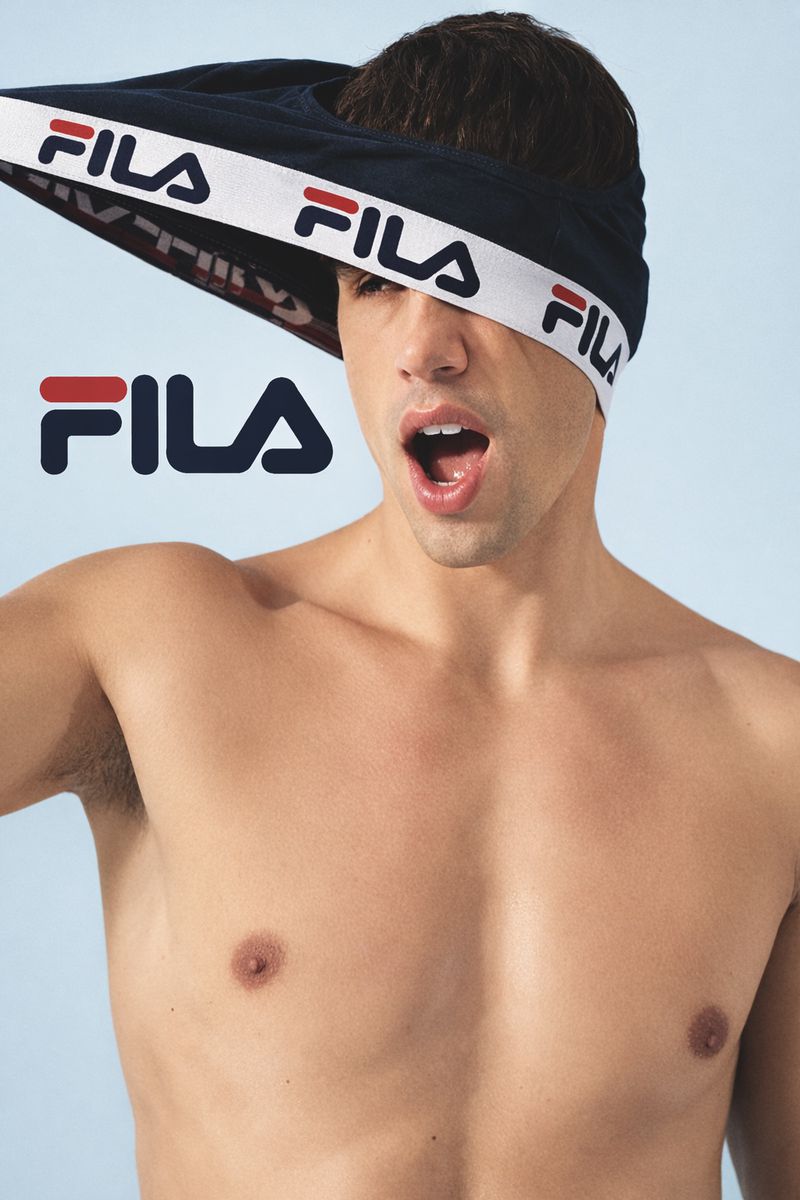A shirtless adult male looks up with his mouth open while wearing briefs over his head with the Fila logo visible on the briefs.