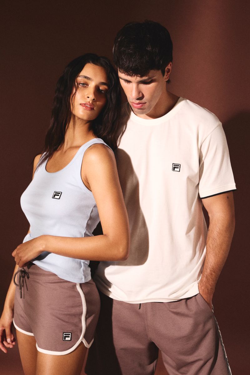 A young couple wearing FILA branded athleisure clothing poses in a photo studio with warm lighting and a brown background for a fashion editorial.