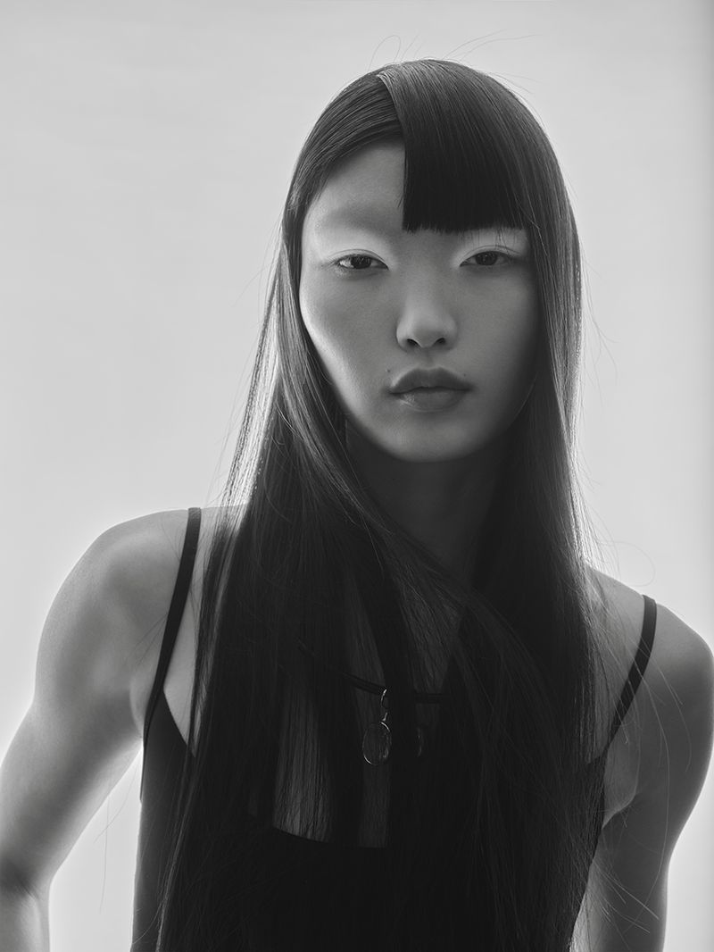 Portrait of an asian woman with long black hair wearing a black top against a bright background in a fashion photography style.