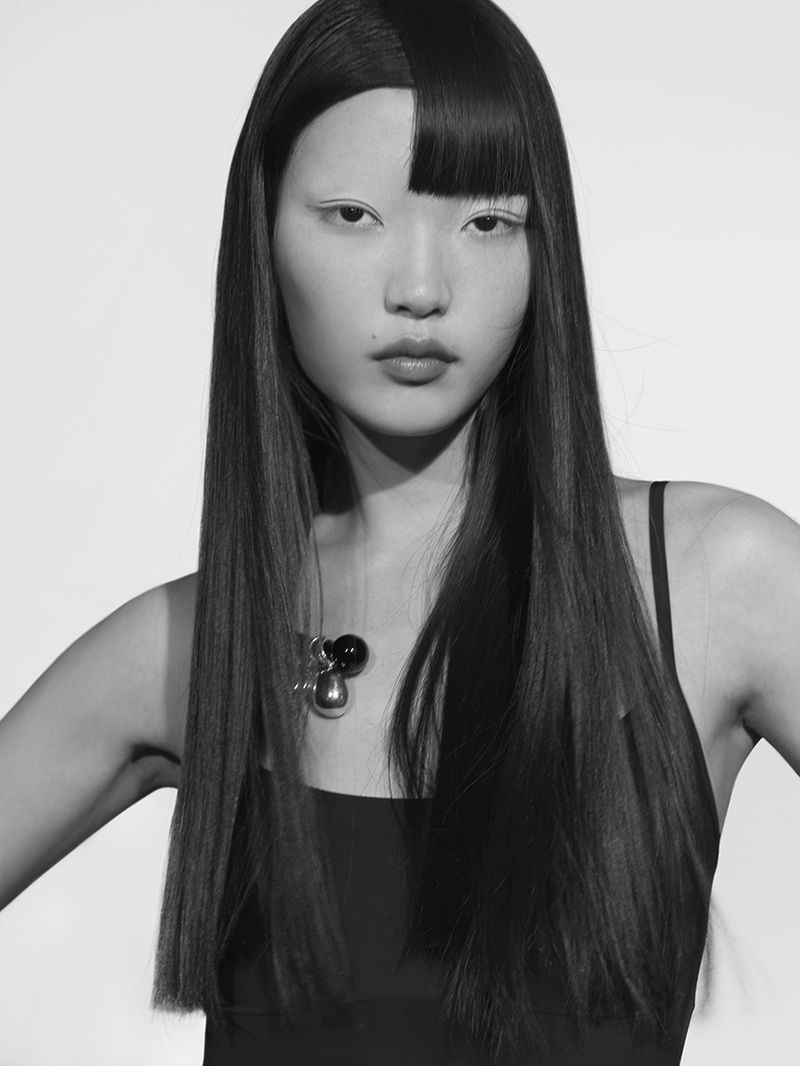Portrait of an Asian adult female model with long black hair and pale eye makeup against a white studio backdrop in black and white.