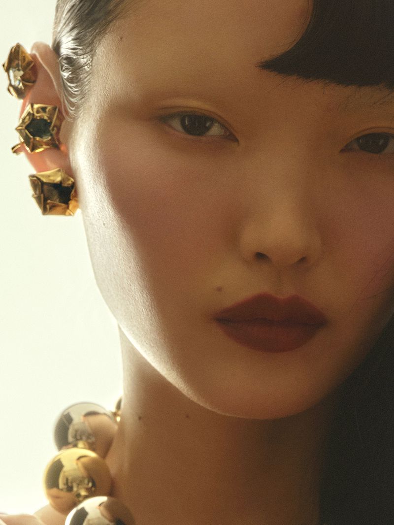 Close-up portrait of an Asian woman with jewel-encrusted ear cuffs and a gold and silver sphere necklace, showcasing beauty and fashion.