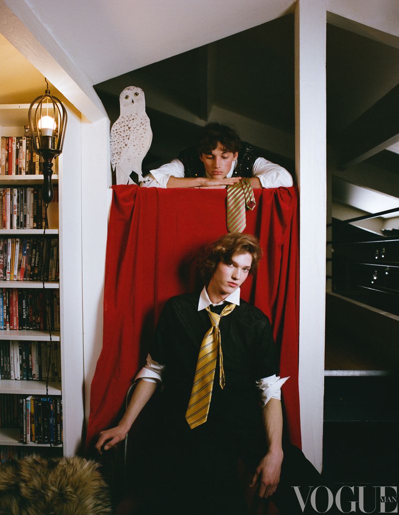 Two young men pose indoors near a bookcase. One man is sitting in a chair behind a red curtain. Vogue Japan logo at the bottom.