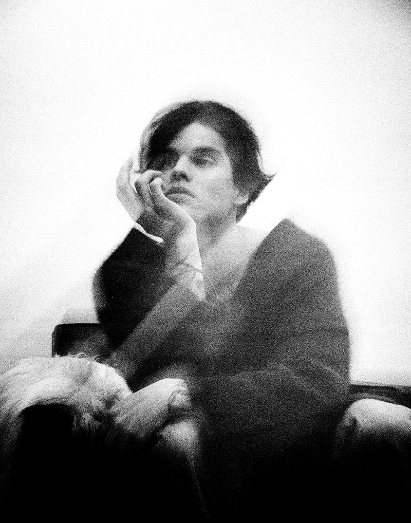 Monochrome portrait of a young adult with short dark hair resting their face on their hand, with a sleeping dog on their lap.
