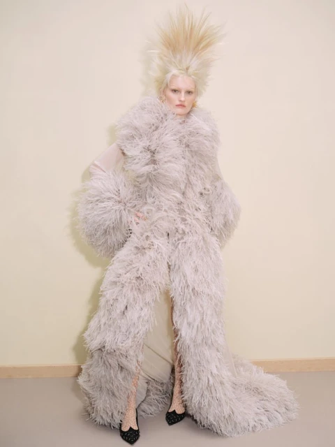 Fashion model with platinum blonde hair and feathery coat poses in studio, showcasing editorial haute couture fashion and dramatic styling.