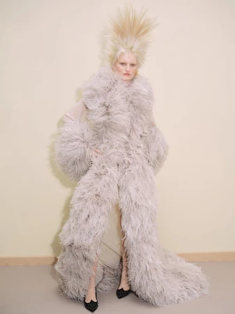 Fashion model with platinum blonde hair and feathery coat poses in studio, showcasing editorial haute couture fashion and dramatic styling.