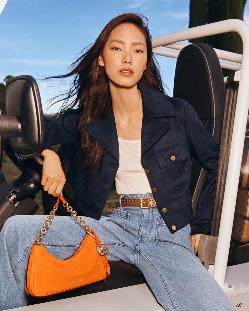 Elegant Asian woman in a car, wearing a blue jacket, holding a trendy orange purse, accessorized with a brown belt, and stylish light blue jeans.
