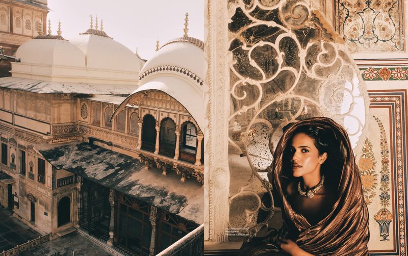 Woman in metallic fabric with an ornate necklace and historic architecture in the background. Architectural details are seen on the facade.