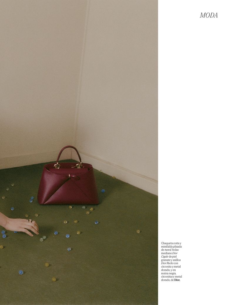 Burgundy leather purse on a green surface with scattered decorative objects and a hand, set against a cream-colored wall.