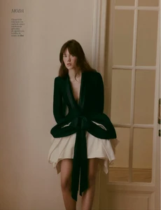 Model wearing a dark green wrap jacket and white skirt standing indoors by a white paneled door for Yo Dona Spain.