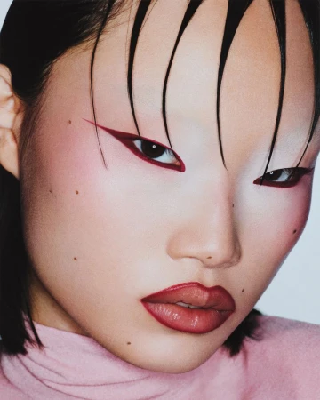 Close-up portrait of an Asian woman with wet, styled hair, distinctive red eyeliner and lipstick, fair skin, and wearing a pink top.