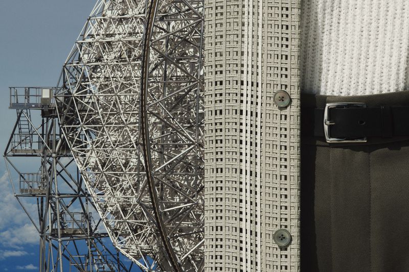 Close-up of a satellite dish antenna against a blue sky, contrasted with a neatly buttoned, patterned coat and black leather belt.