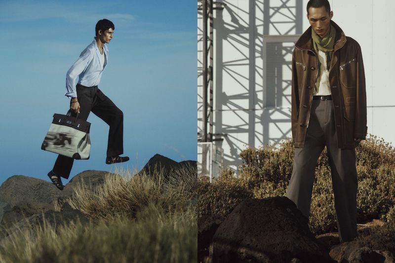 Two fashion models pose outdoors on a rocky landscape, one wearing a light blue shirt and carrying a large bag, the other in brown coat.