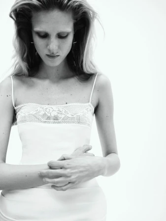 Black and white portrait of a slender, fair-skinned adult female with long wavy hair, wearing a white camisole and looking down.
