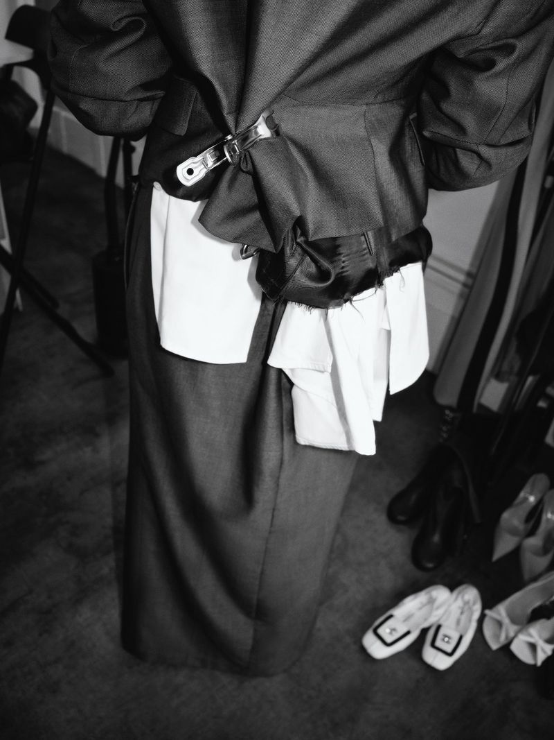 Close-up of a person's back wearing a deconstructed grey suit jacket with white and black accents, paired with a long grey skirt.