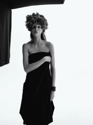 Monochrome studio portrait of a model wearing a textured faux-fur hat and strapless black dress against a plain white background.