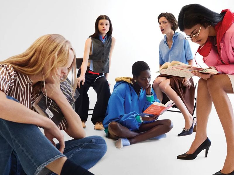 Group of six young adult fashion models sit in a circle reading books, fashion editorial photography, studio lighting, white background.
