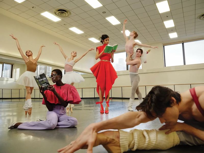 Several ballet dancers, some in traditional tutus and others in casual or fashionable attire, perform in a dance studio.