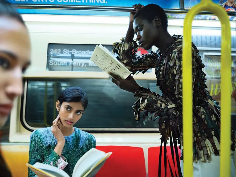 Editorial fashion shot on a subway train featuring three women with unique outfits and diverse looks, reading books and interacting.