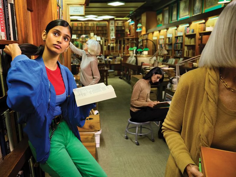 Young woman reading in a vintage library with rows of books and classic architectural details, enhanced by natural light and muted colors.