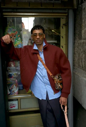 Mohamed Hassan wearing a red jacket and striped shirt standing in a doorway for Louis Vuitton One Fine Day by Cedric Buchet