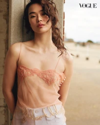 Model Lin Xiangxiang wearing a sheer peach lace camisole leaning against a pillar for Vogue Thailand