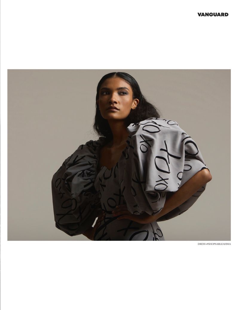Elegant fashion portrait of a woman in a grey patterned dress with oversized sleeves, posing in a photo studio with soft lighting.