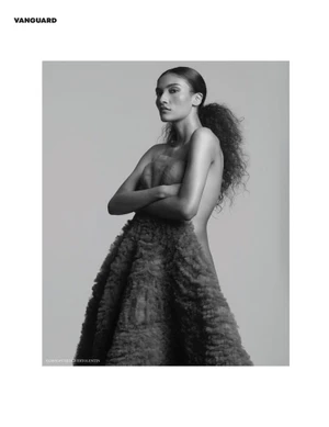 Model in a textured strapless gown with curly hair tied back posing against a plain grey background for Vanguard Magazine.