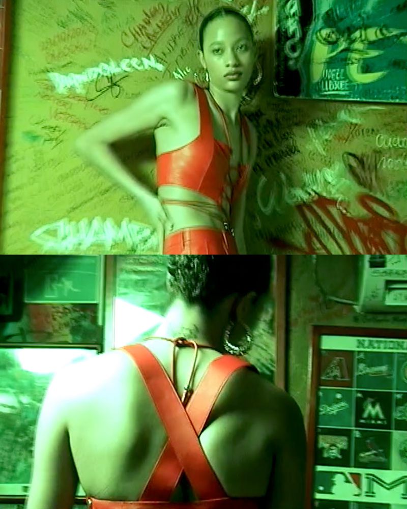Young woman poses in a red crop top and pants against a graffiti wall in a high-fashion setting with a focus on style and visual impact.