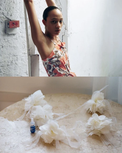Woman in a floral dress poses in front of a textured wall. Floral hair accessories and an adhesive bottle sit on a textured table.