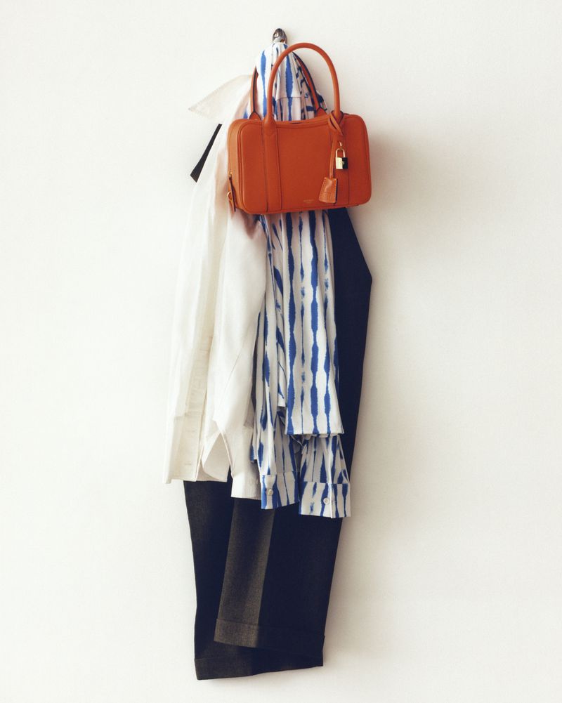 Orange purse hanging on a silver hook with a white collared shirt, white and blue patterned scarf, and black pants.
