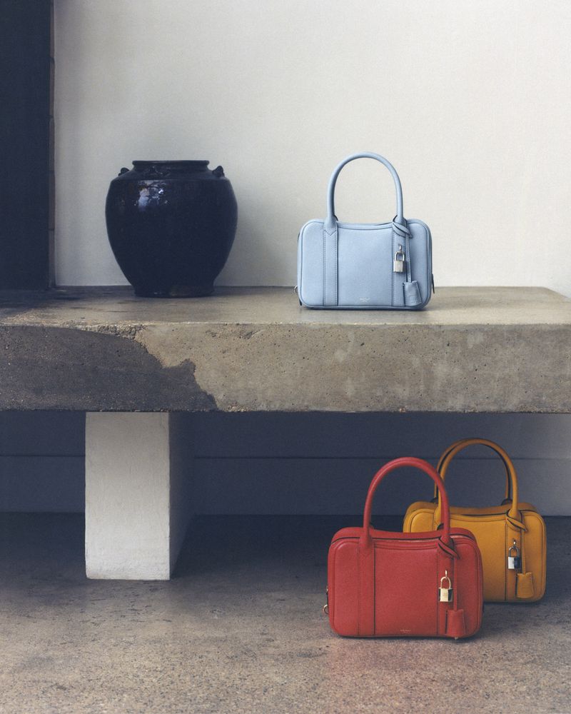 Fashion still life featuring three handbags in blue, red, and yellow, arranged on a concrete surface with a black vase.