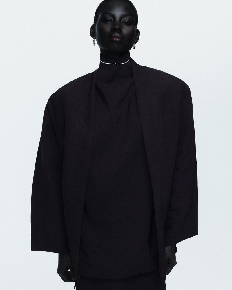 Fashion shot of a Black female model in an oversized black blazer and turtleneck against a clean white backdrop in a photo studio.