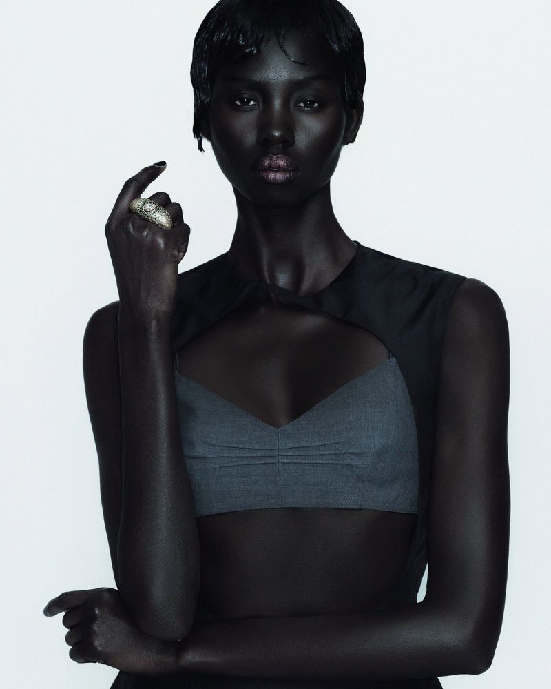Close-up portrait of a Black female adult model in a gray top with a cut-out design, against a white backdrop, with a neutral facial expression.