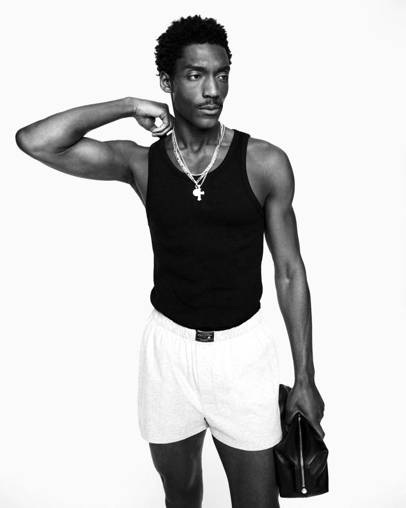 Black and white studio shot of an African American male model in a tank top and shorts, posing with a jacket.