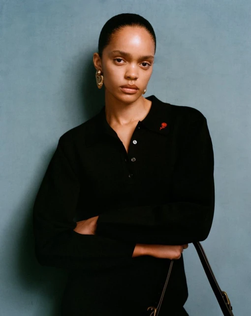 Portrait of a woman with dark hair and wearing a black top with a small rose embellishment, set against a blue background.