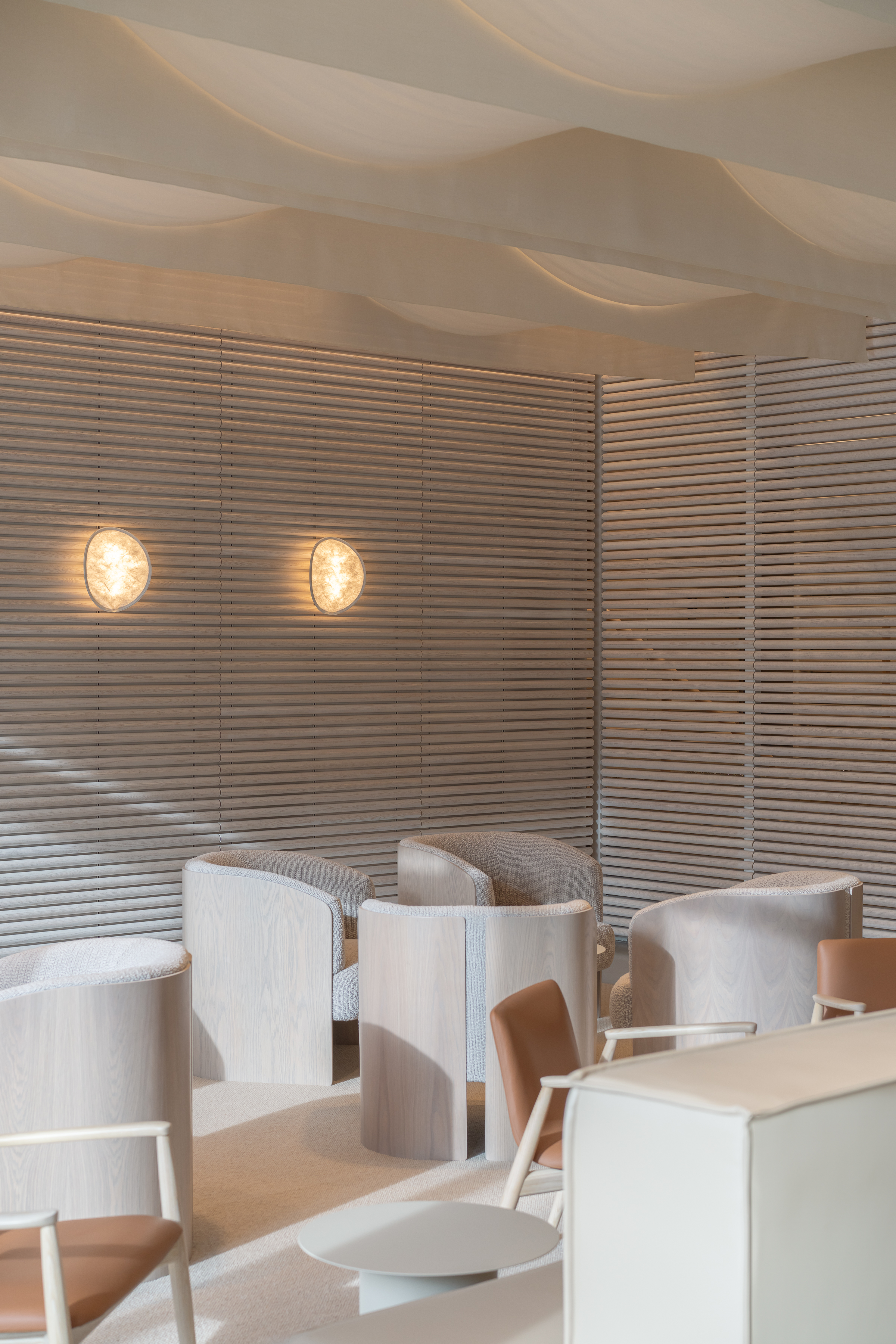 Interior design of a lounge area with light-colored chairs, wall lamps, and wooden wall paneling, creating a bright and inviting space.