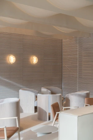 Interior design of a lounge area with light-colored chairs, wall lamps, and wooden wall paneling, creating a bright and inviting space.